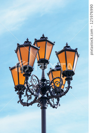 Historic street lamp illuminates urban landscape against clear blue sky. Historic street lamp illuminates urban landscape against clear blue sky. 125976990