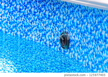 Bright blue mosaic design of pool liner reveals drainage opening in clear water 125977403