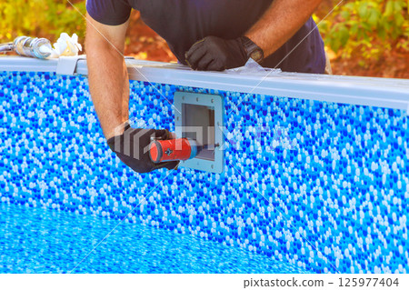 Worker is fixing pool filtration system equipment by edge of blue patterned swimming pool 125977404