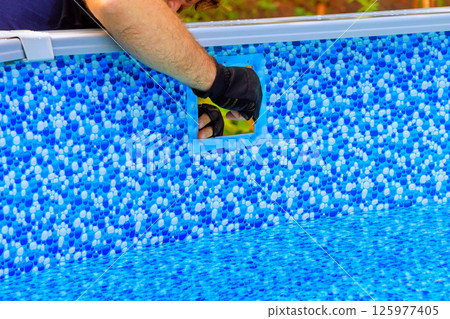 Worker carefully installs component into filtration system newly set up above ground pool on swimming pool backyard setting 125977405
