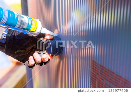 Worker seals connection on pool liner with caulking gun at construction site. Worker seals connection on pool liner with caulking gun at construction site. 125977406