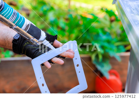 Individual applies sealant to frame frame filter tank system fot swimming pool at backyard 125977412