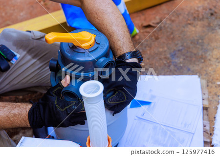 Worker in gloves conducts maintenance on pool filtration system, ensuring proper function cleanliness near swimming pool 125977416