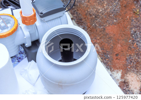 Installation process shows filtration system component ready for connection in swimming pool backyard setting. 125977420