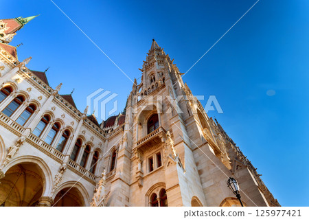 Gorgeous towering architecture of Hungarian Parliament building shines in sunlight against bright blue sky. Gorgeous towering architecture of Hungarian Parliament building shines in sunlight against bright blue sky. 125977421