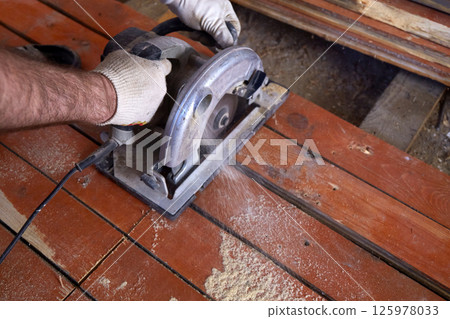 A construction worker uses a circular saw to cut wooden planks in a workshop A construction worker uses a circular saw to cut wooden planks in a workshop 125978033