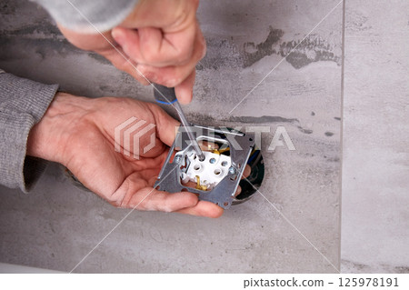 A worker installs an electrical outlet into a wall using a screwdriver A worker installs an electrical outlet into a wall using a screwdriver 125978191