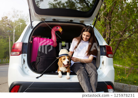A young girl and a beagle dog are sitting in the trunk of a car. 125978231