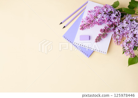A notebook, pencils, and lilac branches on a yellow background. 125978446