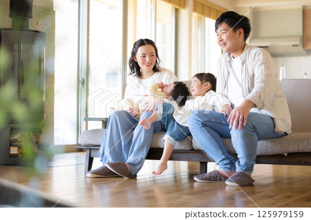 一家四口在一棟新建的、溫暖的木質室內房屋裡的沙發上休息。 125979159