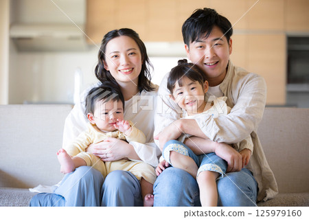 一個日本四口之家在溫暖的木屋裡,坐在沙發上,微笑著看著鏡頭 一個日本四口之家在溫暖的木屋裡,坐在沙發上,微笑著看著鏡頭 125979160