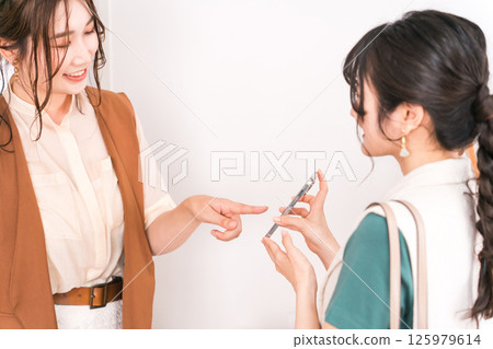 A woman and a shop clerk shopping using smartphones, smartphone payments, and online payments 125979614