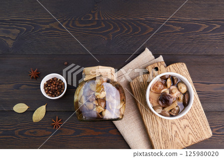 Pickled mushrooms in a glass jar and bowl on dark rustic wooden background. 125980020