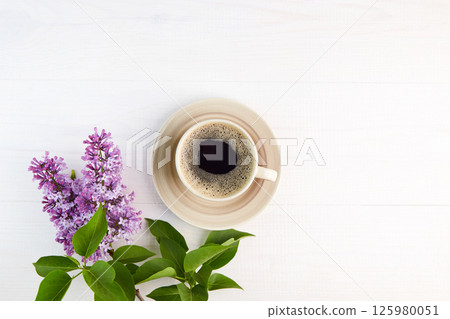 Lilac branches and cup of coffee on a white wooden background. Lilac branches and cup of coffee on a white wooden background. 125980051