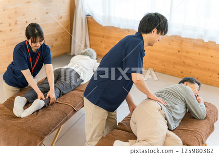 Male and female physical therapists and occupational therapists providing massage and stretching to elderly people as part of rehabilitation Male and female physical therapists and occupational therapists providing massage and stretching to elderly people as part of rehabilitation 125980382