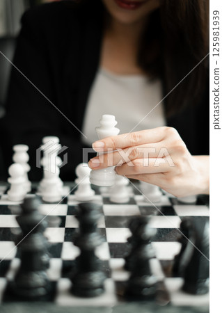 A woman playing chess, focusing on moving a white piece on a classic black and white board, highlighting strategy and concentration. 125981939