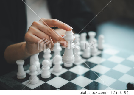 A close-up image of a hand holding a white chess piece, poised over a chessboard, symbolizing strategy and decision-making. A close-up image of a hand holding a white chess piece, poised over a chessboard, symbolizing strategy and decision-making. 125981943