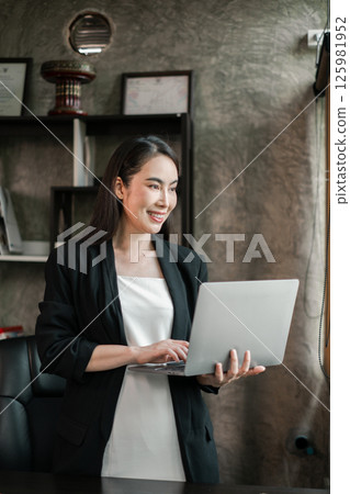 Confident businesswoman using a laptop in a contemporary office environment, showcasing productivity and professionalism. 125981952