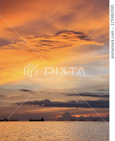 Stunning sunset over calm waters with distant ships at sea near the coastline Stunning sunset over calm waters with distant ships at sea near the coastline 125982095