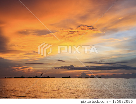 Stunning sunset over calm waters with distant ships at sea near the coastline Stunning sunset over calm waters with distant ships at sea near the coastline 125982096
