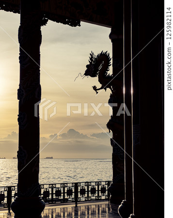 Golden sunset casts a golden glow over the ocean, with decorative columns and a dragon sculpture accentuating the coastal landscape Golden sunset casts a golden glow over the ocean, with decorative columns and a dragon sculpture accentuating the coastal landscape 125982114