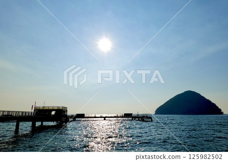 A scene of the setting sun casting a silver band over the sea surface between the pier at Asamushi Sea Fishing Park and Yunoshima Island, Aomori City, Aomori Prefecture 125982502