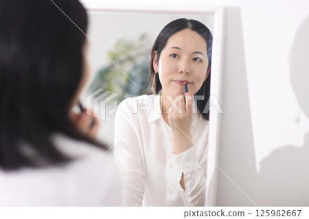 Middle-aged woman putting on lipstick in front of a mirror 125982667
