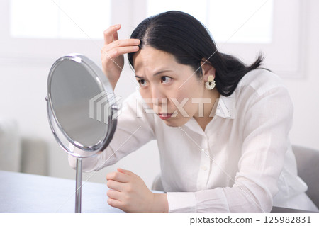 A middle-aged woman who is concerned about her hairline in the mirror 125982831