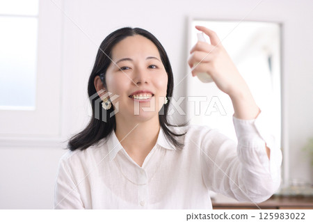A smiling middle-aged woman spraying moisturizing spray on her face 125983022