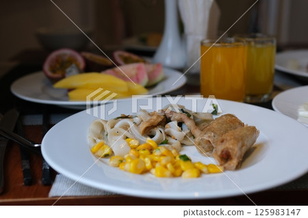 on a white plate lunch dinner corn rice vermicelli with soy meat and two fried spring rolls mango and passion fruit juice as well as fruits for breakfast at the hotel buffet 125983147