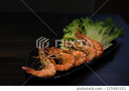 Grilled skewer shrimps and fresh vegetables served on black stony plate on wooden table 125983181