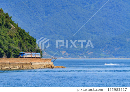 A tourist train on the Kure Line running along the coastline with the deep blue Seto Inland Sea in the background 125983317