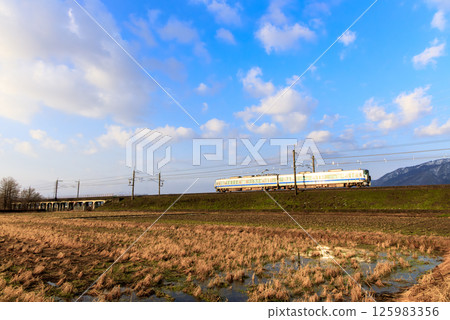 A local train running through fallow fields in winter, reflecting the morning sun A local train running through fallow fields in winter, reflecting the morning sun 125983356