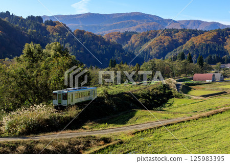 一列行駛在飯山線上的柴油列車穿過青倉地區,背景是秋色的山脈 一列行駛在飯山線上的柴油列車穿過青倉地區,背景是秋色的山脈 125983395