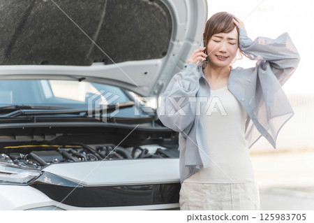Asian woman calling on smartphone in front of car (road service, trouble, rescue, trouble) Asian woman calling on smartphone in front of car (road service, trouble, rescue, trouble) 125983705