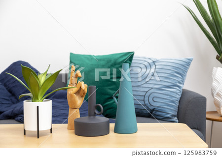 Stylish living room interior with orange, blue, red pillow on sofa, wooden coffee table and olive tree in a pot. 125983759
