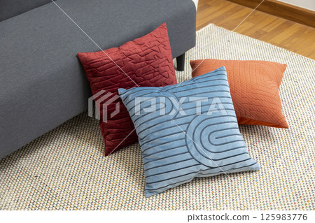 Stylish living room interior with orange, blue, red pillow on sofa, wooden coffee table and olive tree in a pot. 125983776
