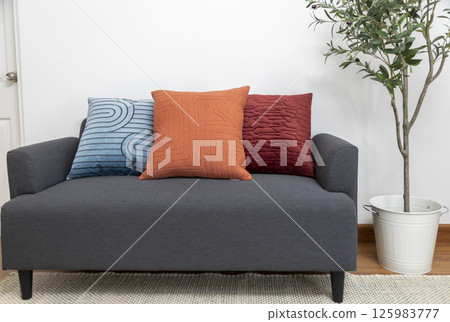 Stylish living room interior with orange, blue, red pillow on sofa, wooden coffee table and olive tree in a pot. Stylish living room interior with orange, blue, red pillow on sofa, wooden coffee table and olive tree in a pot. 125983777