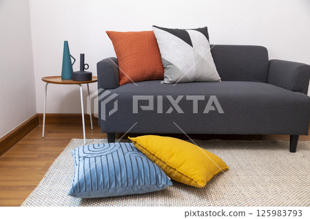 Stylish living room interior with orange, red blue, yellow pillow on sofa, wooden coffee table and olive tree in a pot. 125983793
