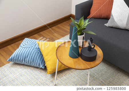 Stylish living room interior with orange, red blue, yellow pillow on sofa, wooden coffee table and olive tree in a pot. 125983800