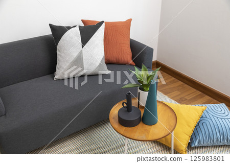 Stylish living room interior with orange, red blue, yellow pillow on sofa, wooden coffee table and olive tree in a pot. Stylish living room interior with orange, red blue, yellow pillow on sofa, wooden coffee table and olive tree in a pot. 125983801