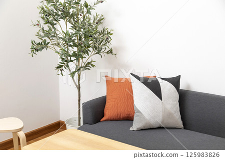 Stylish living room interior with orange, blue, yellow pillow on sofa, wooden coffee table and olive tree in a pot. Stylish living room interior with orange, blue, yellow pillow on sofa, wooden coffee table and olive tree in a pot. 125983826