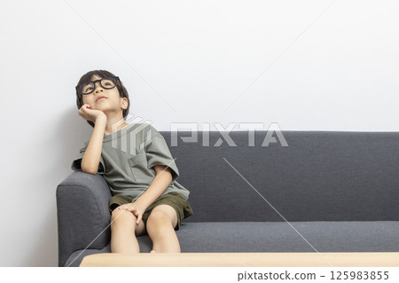 Cute Asian boy with eyeglasses sitting on a sofa at home. 125983855