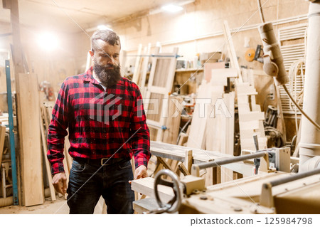 Skilled carpenter working in a workshop surrounded by wood and tools during the day Skilled carpenter working in a workshop surrounded by wood and tools during the day 125984798