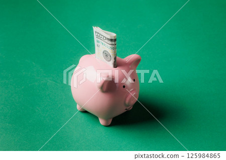 Piggy bank with dollar bill inserted on a bright green background illustrating savings concept 125984865