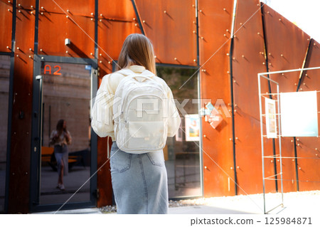 Woman walking towards creative art building with large backpack in sunny urban setting 125984871