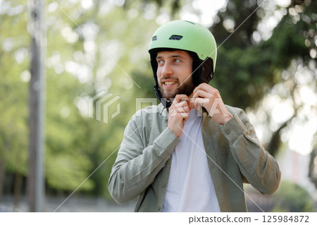 Young man prepares for cycling in park while smiling and wearing a green helmet during sunny afternoon 125984872
