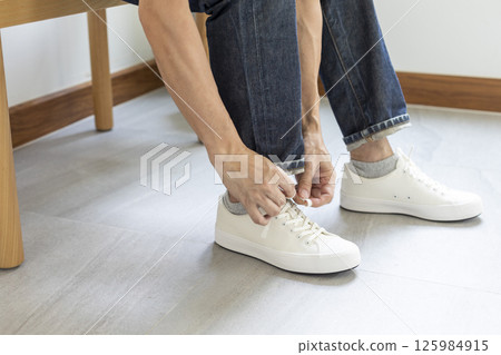Man tie the shoelace of white sneakers sit on wood bench at home. 125984915