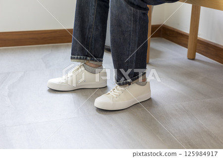 Man tie the shoelace of white sneakers sit on wood bench at home. 125984917
