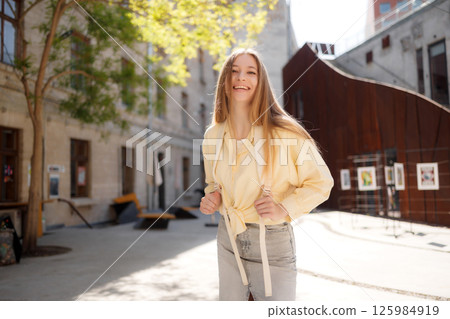 Young woman smiling in light clothing enjoys a sunny day in an urban courtyard with art installations 125984919
